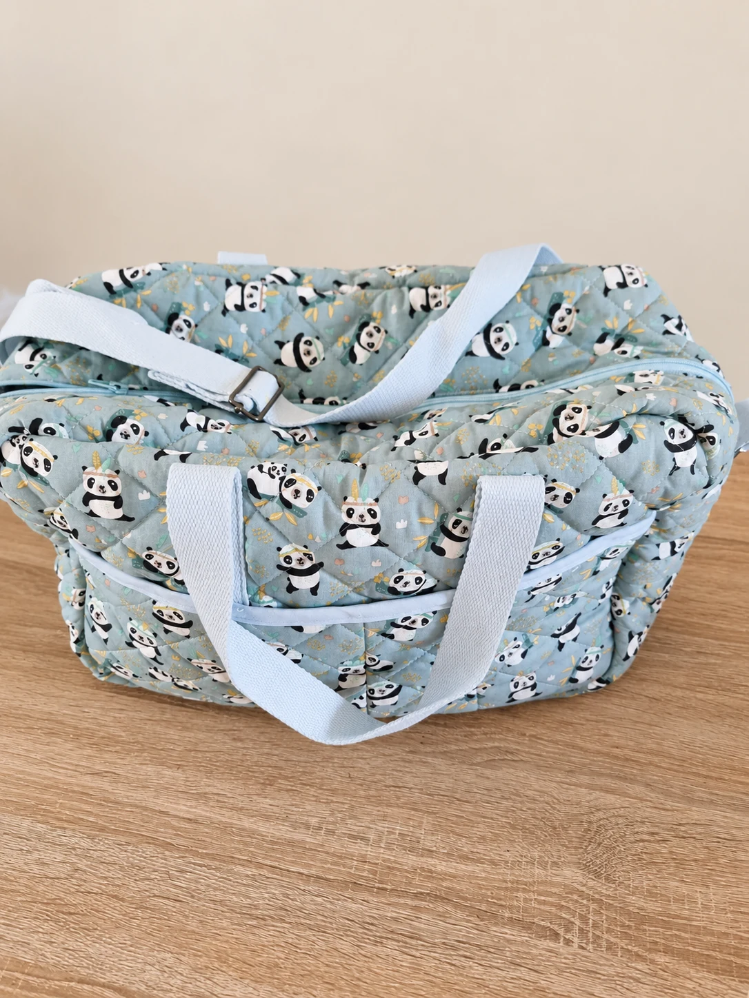 Sac bébé à motifs de pandas sur fond bleu et vert pâle, avec des anses et une bandoulière blanches