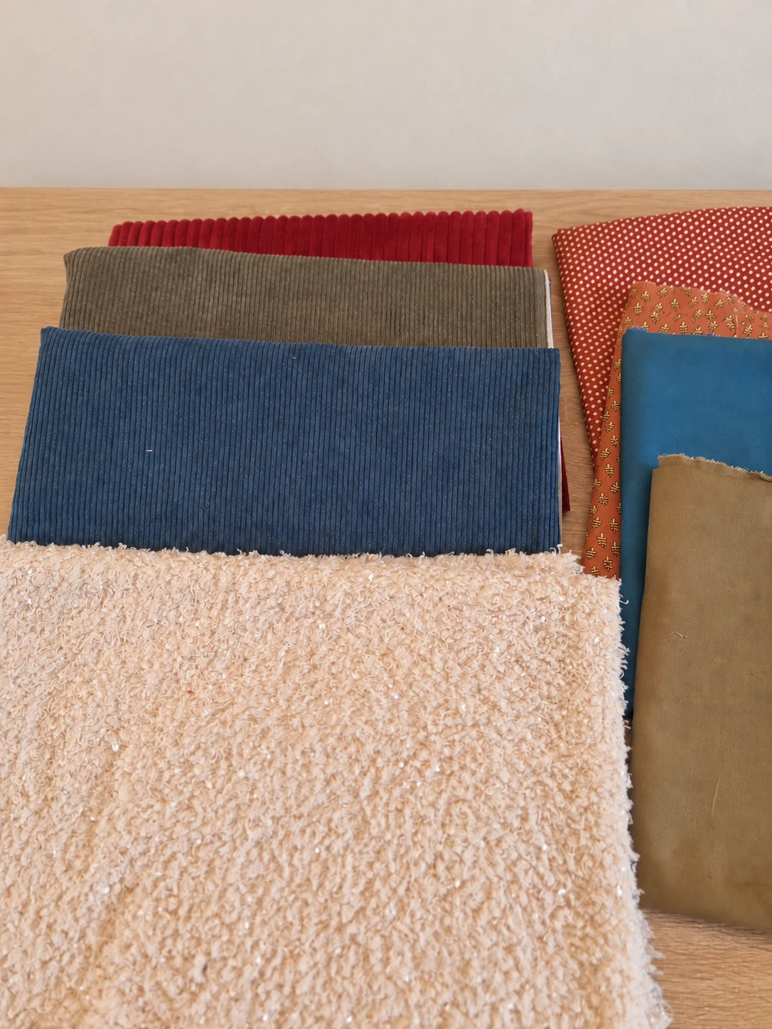 Échantillons de tissus unis et imprimés, dont des velours côtelés bleus, verts et rouges et un tissu écru texturé